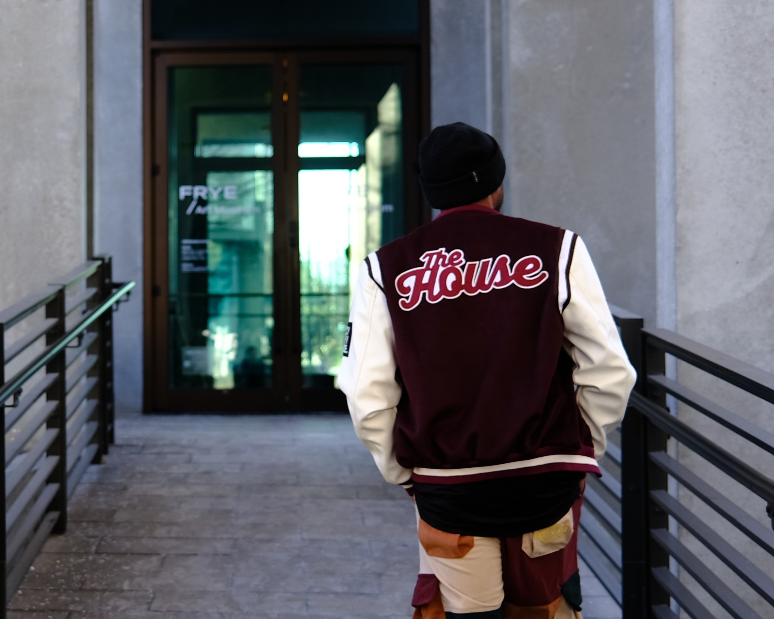 Chris Carthern walking toward glass doors in his Morehouse College 'The House' varsity jacket, symbolizing his journey from educational foundation to creative future